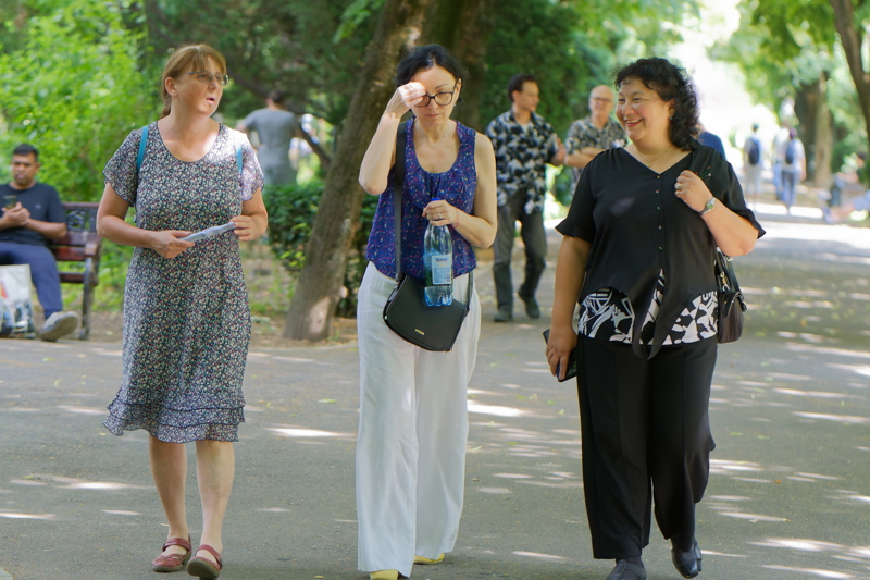 18 - Three women walking along a paved path in a lush, green park